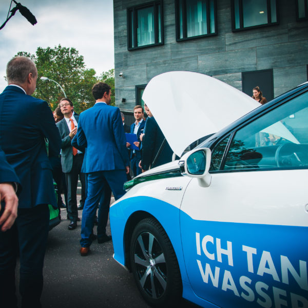 NIP Bescheiduebergabe Bundesverkehrsminister Scheuer und Personen stehen vor einem Wasserstoff-Pkw