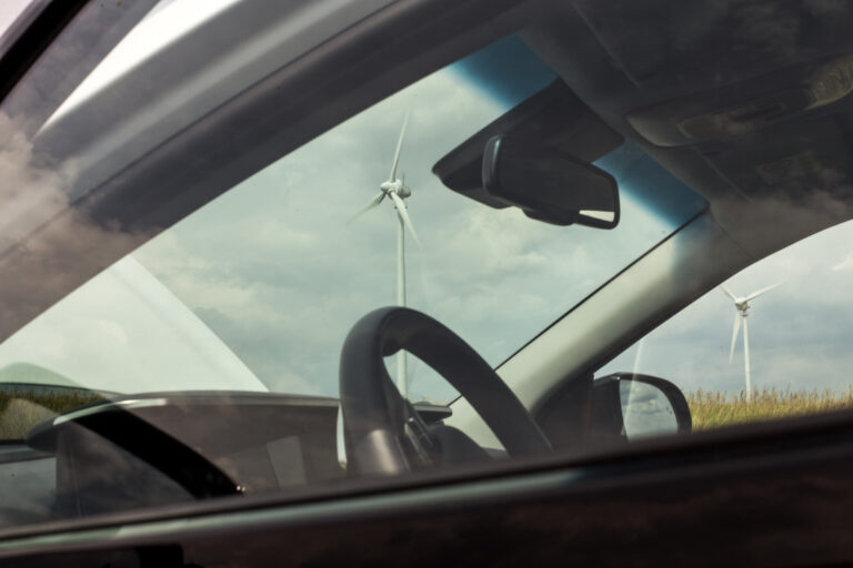 Blick durch die Scheibe eines E-Autos auf ein Windrad